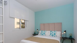 Une chambre à coucher comprenant un lit, deux tables de chevet, une fenêtre et un climatiseur fixé au mur.