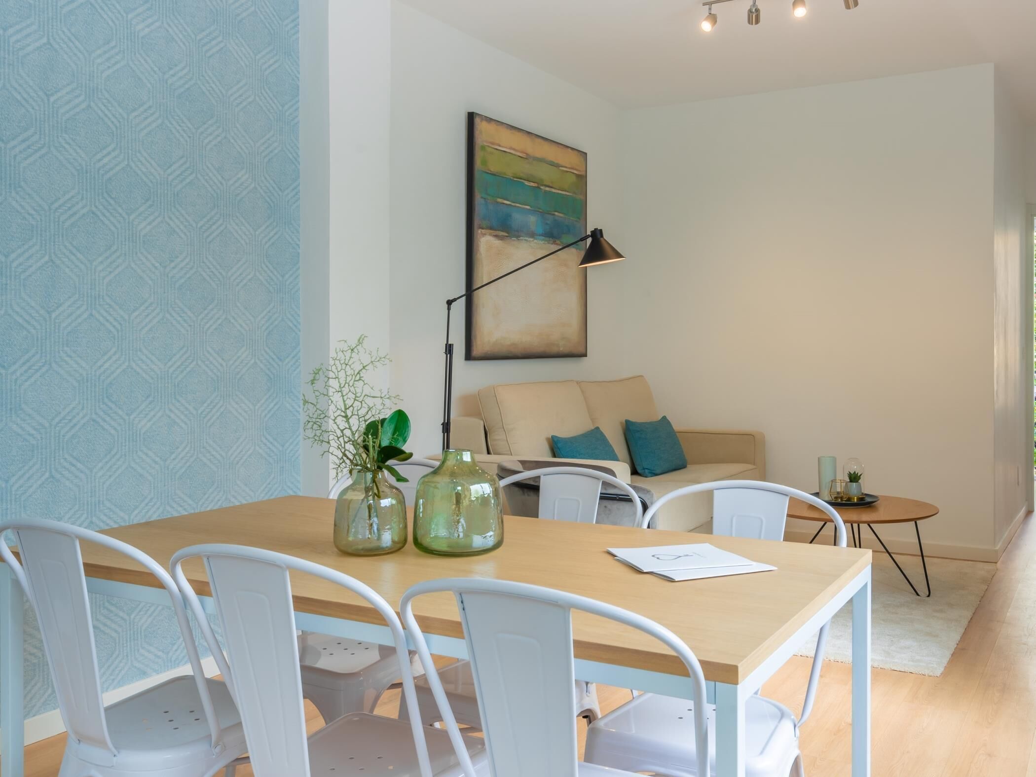 Un coin repas avec une table en bois, des chaises blanches et deux vases en verre vert contenant des plantes.