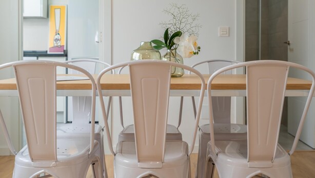 Un coin repas avec une table en bois et des chaises blanches. Un vase rempli de fleurs est posé sur la table.