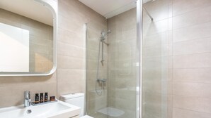 Une salle de bain moderne avec une douche à parois de verre, un lavabo blanc avec des articles de toilette et des toilettes.