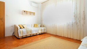 A bedroom with a bed, wooden floor, a window with sheer curtains, and a wall-mounted air conditioner. - Apartment 1804/21276 (Istria - Medulin), 500m from the beach (Medulin)