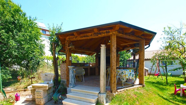 A wooden gazebo with a table and chairs, surrounded by a garden with potted plants and a swing set. - Apartment 1804/21276 (Istria - Medulin), 500m from the beach (Medulin)