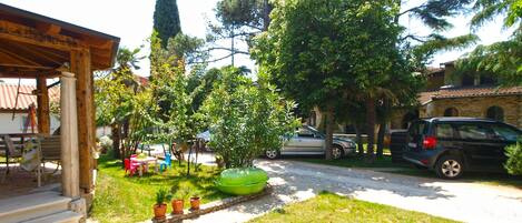 A courtyard with a covered seating area, a pathway lined with potted plants, and parked cars.