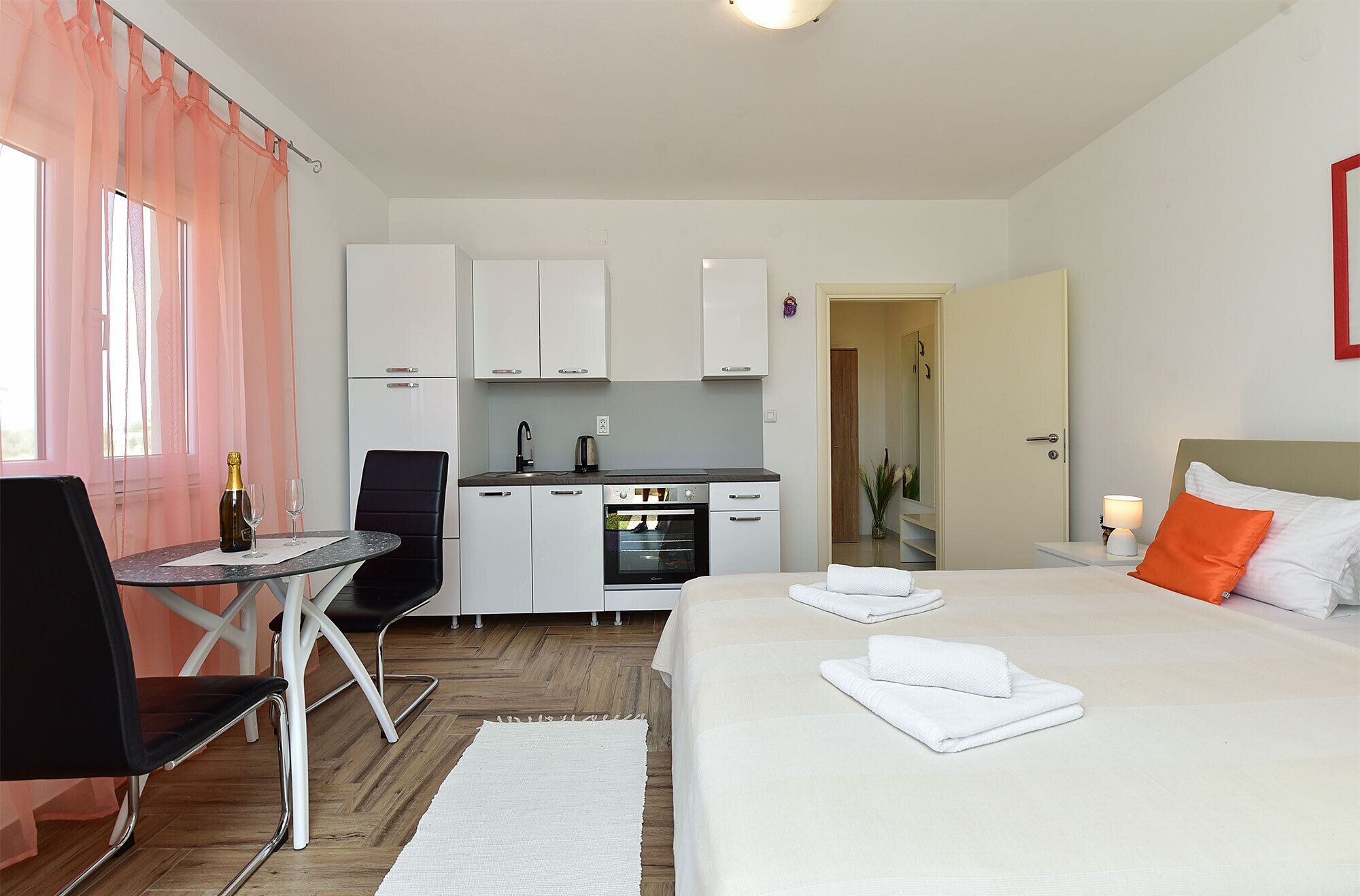 Ein Hotelzimmer mit einem Bett, einem kleinen Esstisch mit Stuhl, einer Küchenzeile und einem durch eine offene Tür einsehbaren Badezimmer.