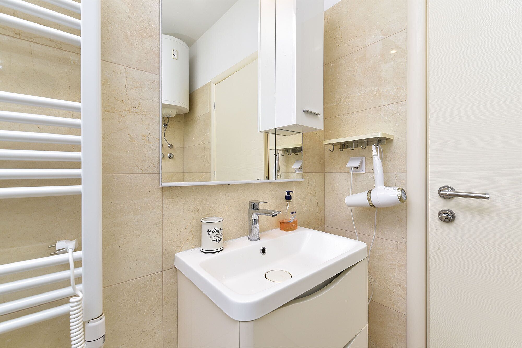 Une salle de bain avec un lavabo blanc, un miroir, un porte-serviettes et une porte.