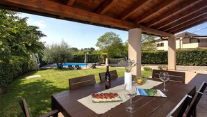 Een terras buiten met een houten eettafel, een fles wijn en een bord eten.