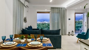 A modern living room with a dining area, a sofa, and a view of a cityscape. - Villa Izabela (Hersonissos)
