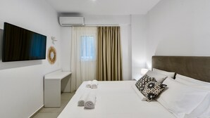 A modern hotel room with a large bed, a bedside table, a flat-screen TV mounted on the wall, and an air conditioning unit. - Villa Izabela (Hersonissos)