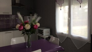 Een keuken met een eettafel, een bloemenvaas, een magnetron en een raam met gordijnen.