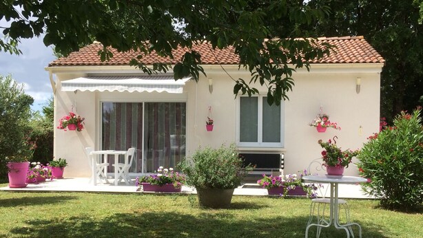 Een huis met pannendak, een overdekte veranda en potplanten.