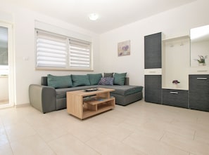 Uma sala de estar moderna com um sofá cinzento, uma mesa de centro de madeira e um armário embutido com espelho.