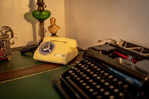 A vintage yellow rotary dial telephone, a black typewriter, and a green glass lamp on a wooden desk.