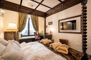 A hotel room with a large bed, a television mounted on the wall, a window with curtains, and a lamp on a bedside table.