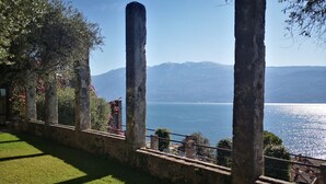 Aussicht auf einen See mit Bergen im Hintergrund, Steinpfeilern und einer grünen Wiese.