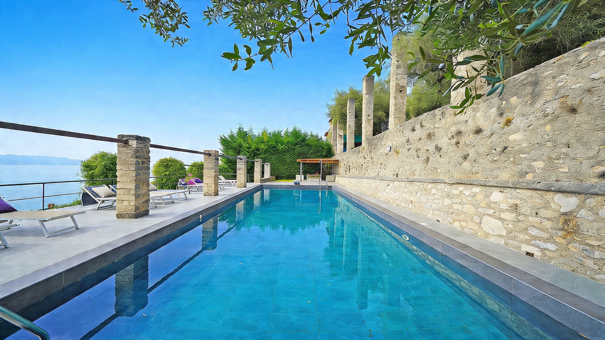 A clear blue pool with stone pillars, a pergola, and a view of the sea.