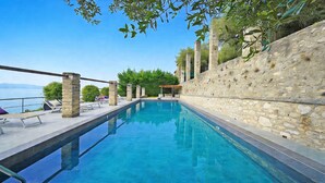 Ein klares, blaues Schwimmbecken mit Steinpfeilern, einer Pergola und Blick aufs Meer.