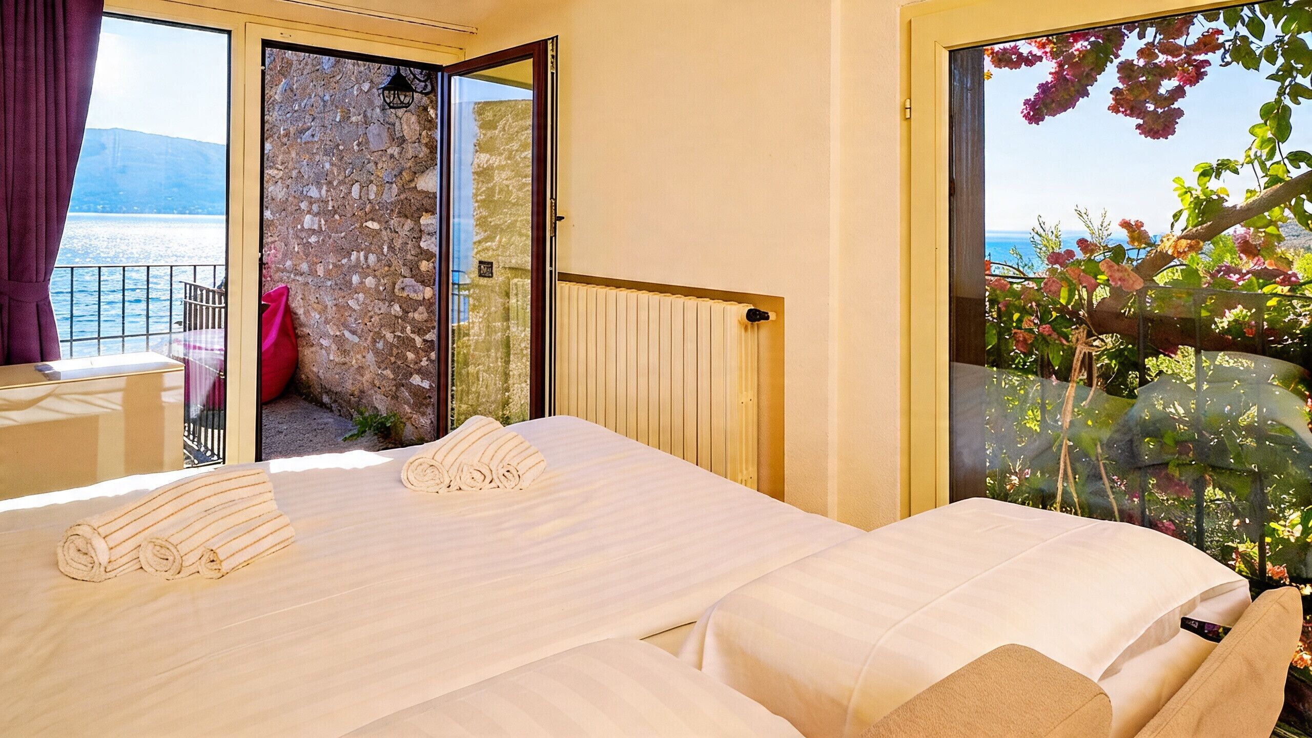 Ein Hotelzimmer mit zwei Betten, Meerblick und einem Balkon mit Stuhl und Tasche.