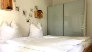 Una cama bien hecha con ropa blanca, un cabecero de madera y una mesita de noche con una lámpara.