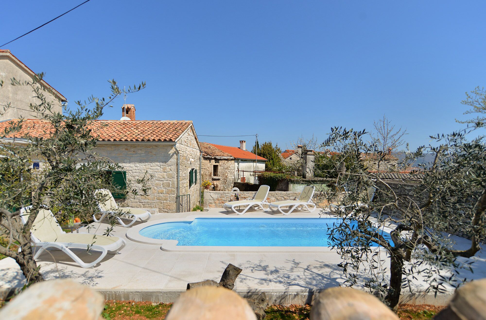 A pool area with lounge chairs, stone buildings, and a clear blue sky.