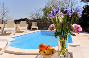 A poolside setting with a clear blue pool, lounge chairs, a vase with flowers and fruit. - House 1829/21736 (Istria - Rakalj), 1500m from the beach (Rakalj)