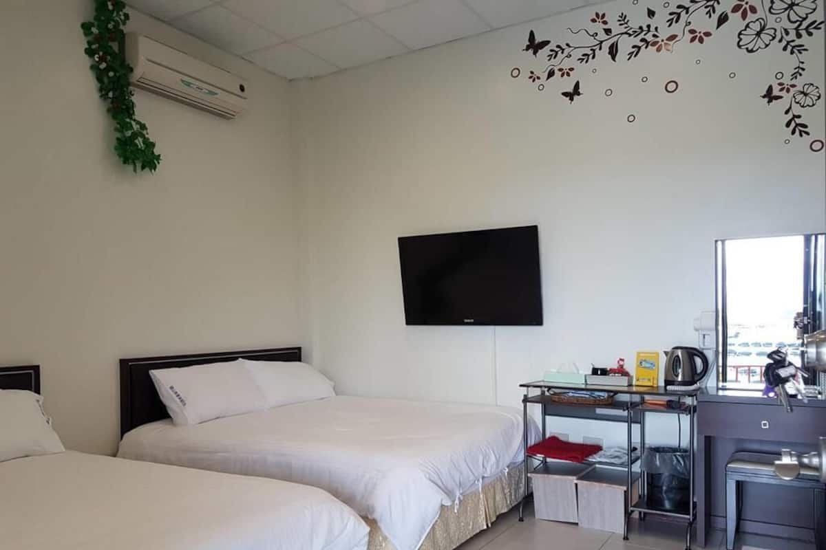 Une chambre d’hôtel avec deux lits, une télévision, un bureau avec une bouilloire et une fenêtre.