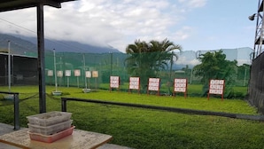Un espacio al aire libre cubierto con una mesa y sillas, rodeado por un recinto verde con mallas y objetivos numerados.