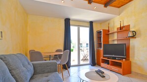 A living room with a sofa, a coffee table, a TV on a wooden stand, and a dining area with chairs and a table. - Apartment 1838/21894 (Istria - Pomer), 400m from the beach (Pomer)