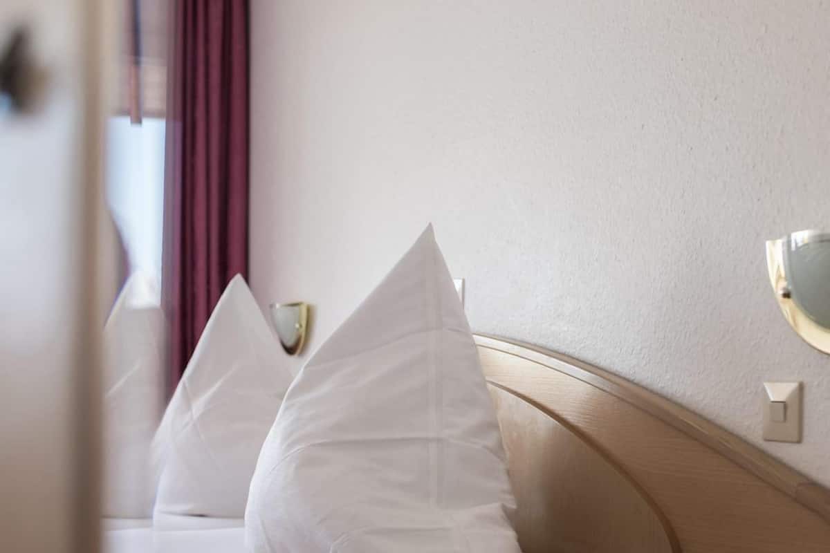 A hotel room with a bed, pillows, bedside table, lamp, and a telephone.