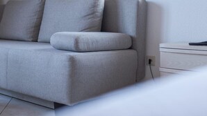 A grey sofa with a matching ottoman in a modern room with a white wall and a window. - Landhotel Bodensee (Konstanz)