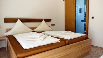 Una cama doble con dos almohadas y toallas dobladas, un cabecero de madera y vistas a un baño con pared de azulejos azules.