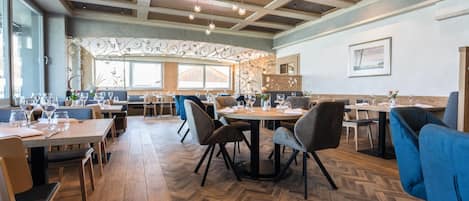 A restaurant interior with wooden flooring, tables, chairs, and hanging pendant lights.