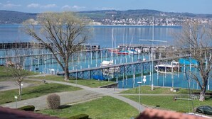 A marina with boats docked, a wooden pier, and a view of a distant town across the water. - Landhotel Bodensee (Konstanz)