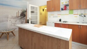 A modern kitchen with wooden cabinets, a white countertop, and a view of the beach through a door.