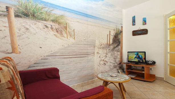 A living room with a beach mural, a red sofa, a small round table, and a television on a wooden stand.