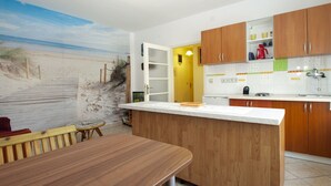 A kitchen with wooden cabinets, a white countertop, and a beach mural on the wall.