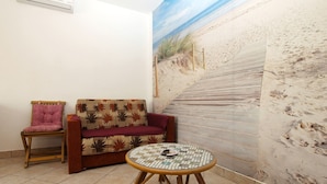 A room with a beach mural, a wooden chair, a sofa, and a small round table.