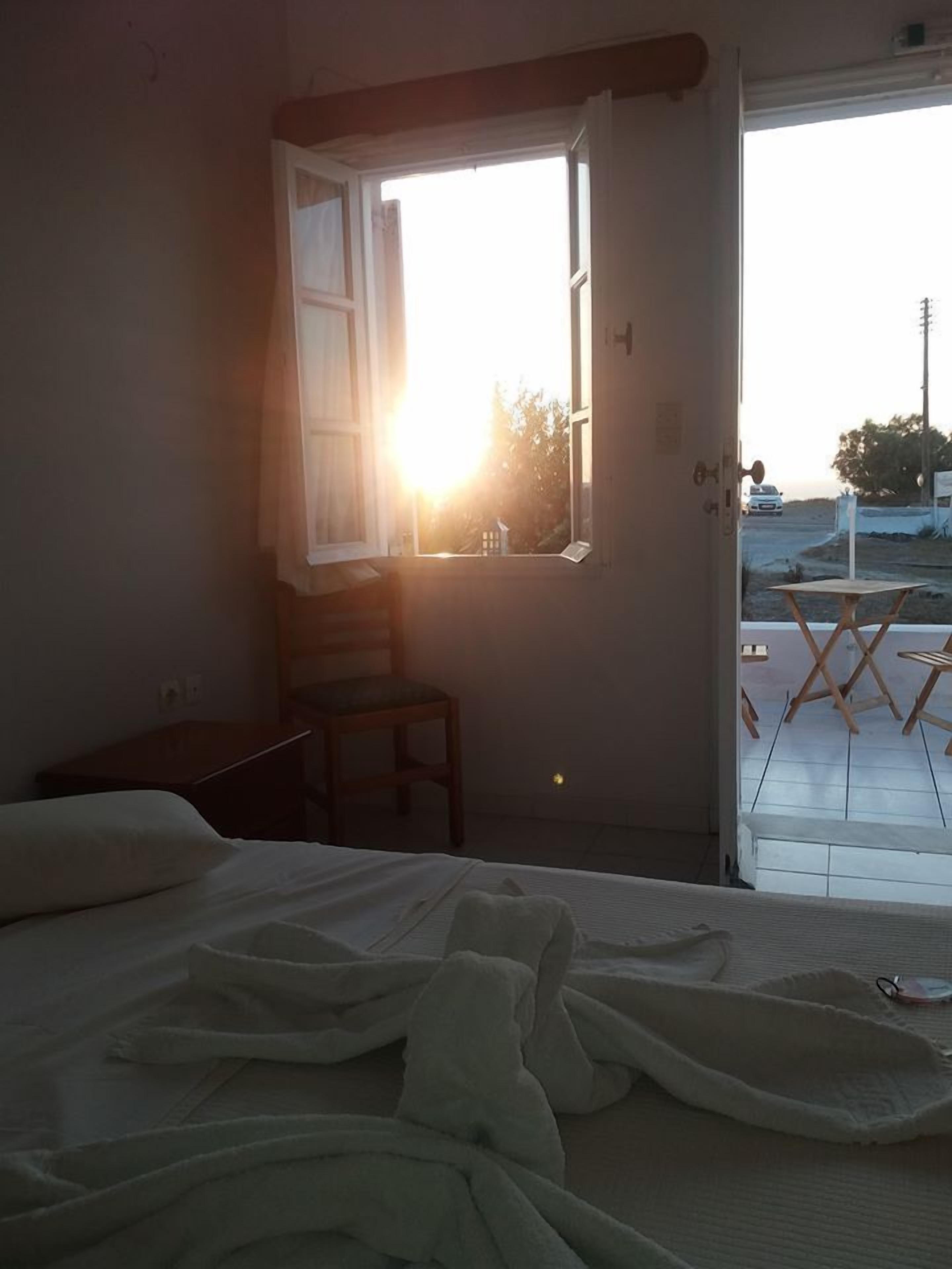 A hotel room with a bed, a chair, a small table, and a window with a view of the outside.