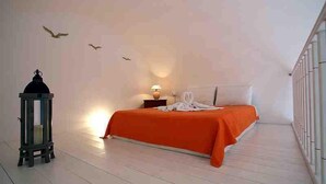 Un dormitorio con cama, mesita de noche, lámpara, estante en la pared y un adorno con forma de pájaro.