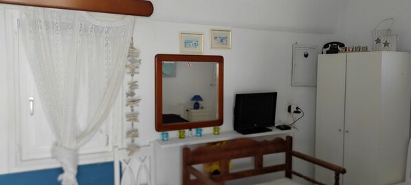 A bedroom with a bed, a desk with a computer, a wardrobe, and a mirror. - Abyssanto Villa (Santorini)