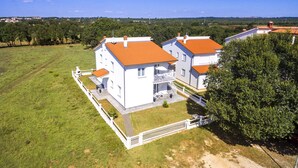 A two-story house with a red roof, surrounded by a white fence, and a grassy yard.