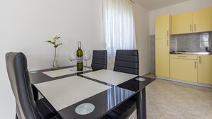 A modern dining area with a black table, four chairs, a vase with a white flower, and a bottle of wine.