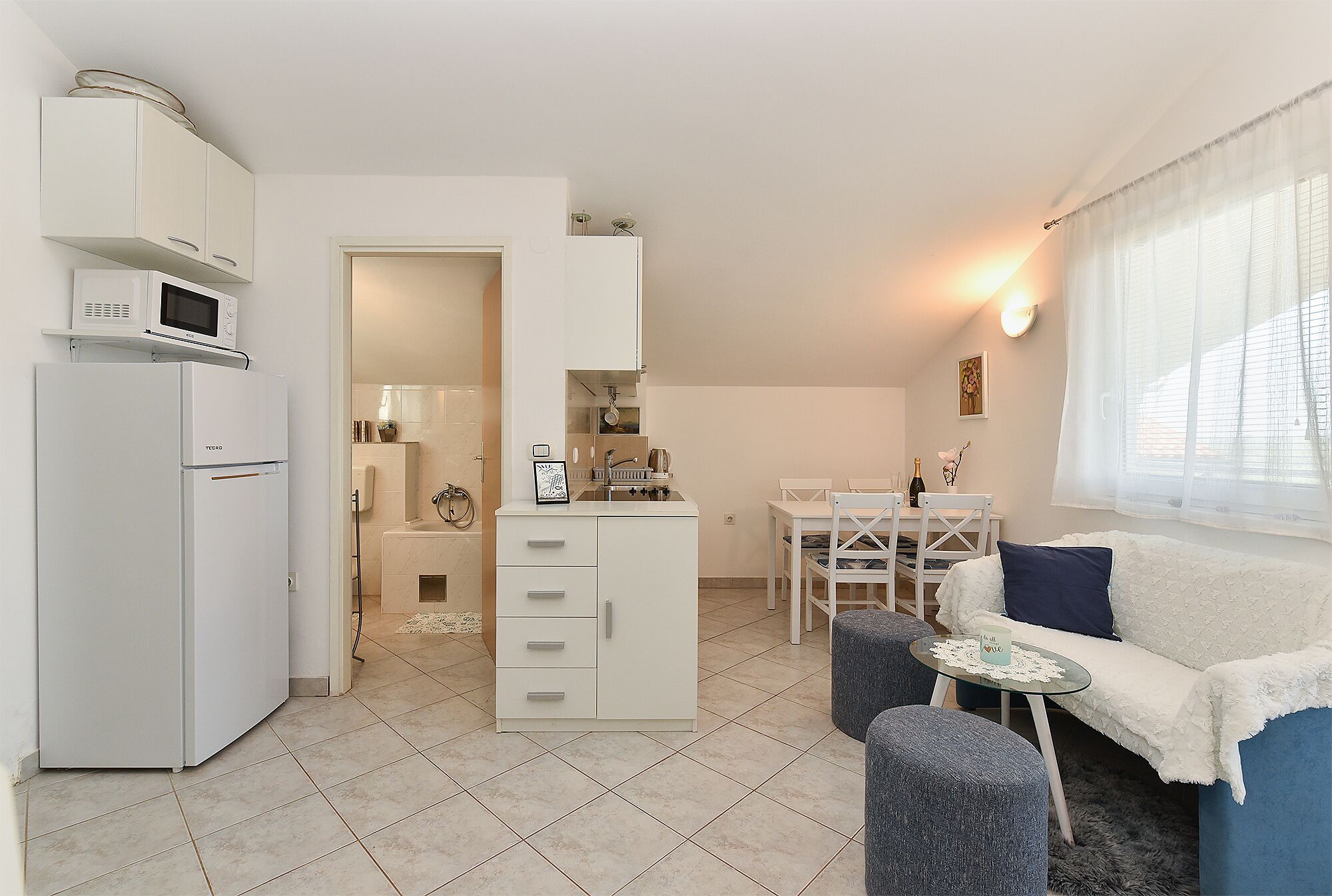 Een compacte leefruimte met een kitchenette, een eetgedeelte en een zithoek met een bank en voetenbankje.