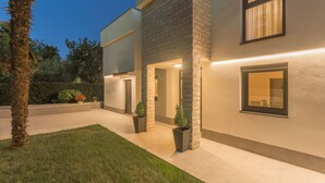 A modern two-story house with a well-lit exterior, a paved driveway, and a small garden area with potted plants and a palm tree. - Villa 1863/22758 (Istria - Poreč), 350m from the beach (Poreč)