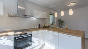 A modern kitchen with white cabinetry, a built-in oven, a stainless steel range hood, and pendant lighting. - Villa 1863/22758 (Istria - Poreč), 350m from the beach (Poreč)