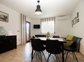 A dining area with a table, chairs, a vase with lemons, a television on the wall, and a sofa. - Apartment 1868/22922 (Istria - Stinjan), 750m from the beach (Stinjan)