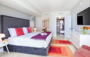A modern hotel room with a large bed, a bedside table, a TV, a bathroom, and a walk-in closet.