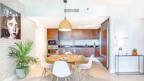 A modern kitchen with a dining area, white walls, and a potted plant. - Brickell Urban Oasis | Modern Apartment (Miami)