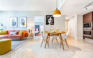A modern living room with a sofa, a dining table with chairs, and a kitchen area with an oven.