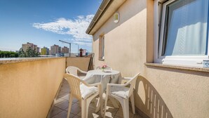 A small balcony with a table and chairs, a window with a curtain, and a view of buildings in the background. - Apartment 1873/23021 (Istria - Pula), 3000m from the beach (Pula)