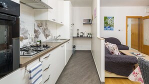 A compact kitchen with a gas stove, microwave, and a small countertop. There is a wooden door leading to a bedroom with a bed and a nightstand. - Apartment 1873/23021 (Istria - Pula), 3000m from the beach (Pula)